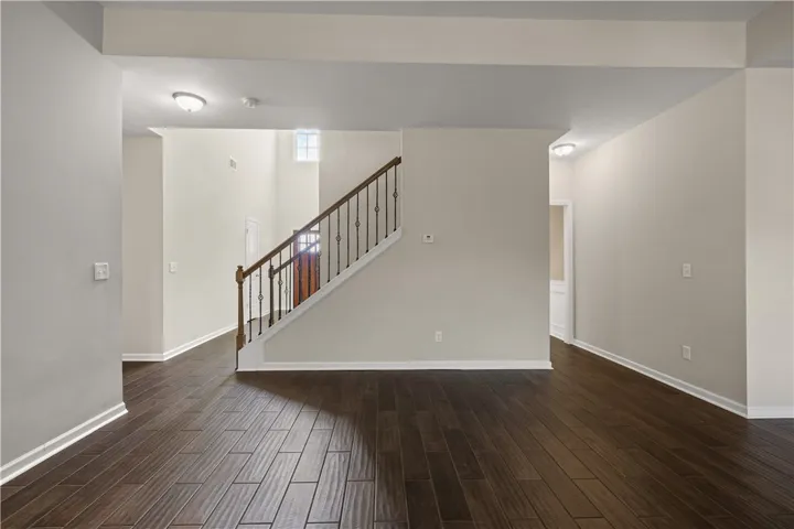 Rich hardwood-style tile flooring guides the eye toward a grand staircase and sun-lit upper landing.