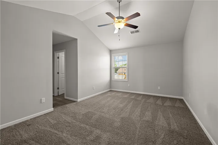 A well-lit bedroom with vaulted ceilings, featuring soft carpeting and a window offering outdoor views.