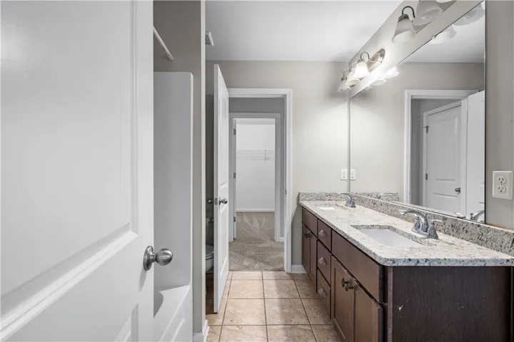 Double vanity with stone counters provides ample space and elegant appeal in this well-appointed bathroom.