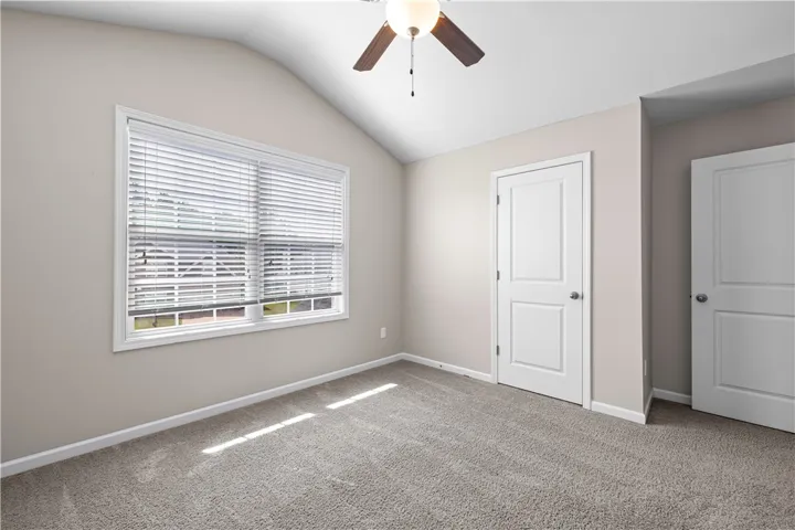 A versatile bedroom with plush carpeting and natural light from a broad window, ideal for restful living.