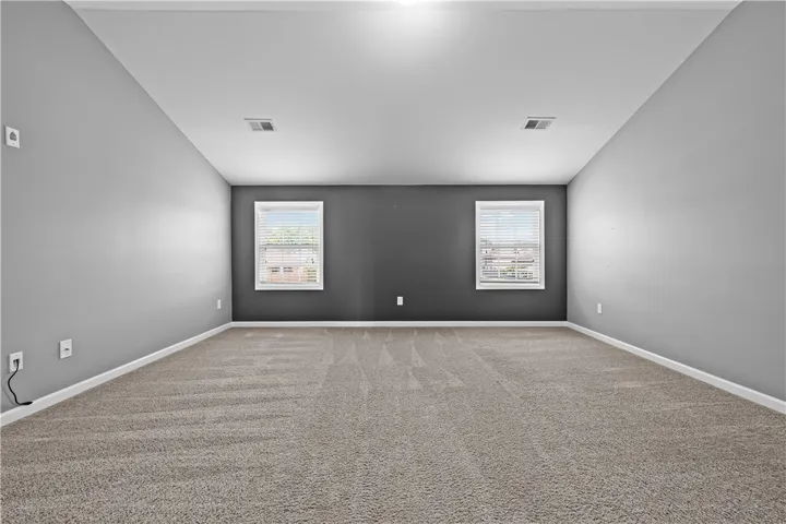 A spacious room offers comfortable carpet flooring and multiple windows, creating a versatile living space.
