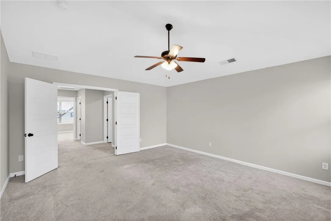 A spacious, naturally illuminated room featuring plush carpet flooring and a modern ceiling fan for comfort.