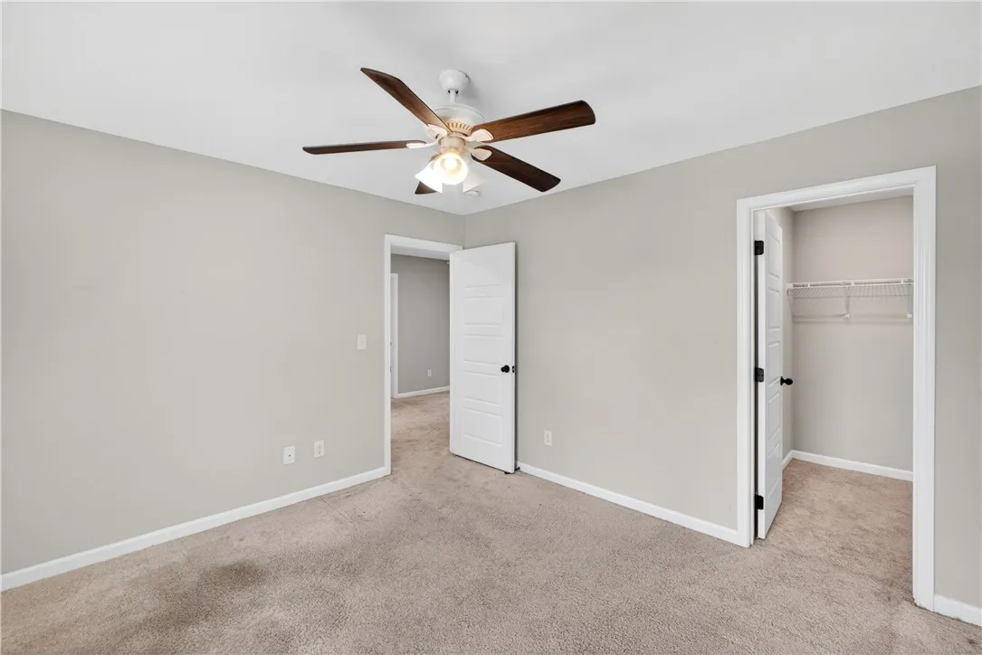 A well-lit room with plush carpeting offers comfort and a ceiling fan for climate control.