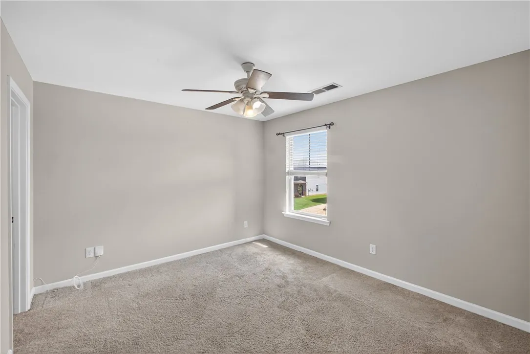 A well-lit bedroom features plush carpeting and a modern ceiling fan, inviting relaxation.