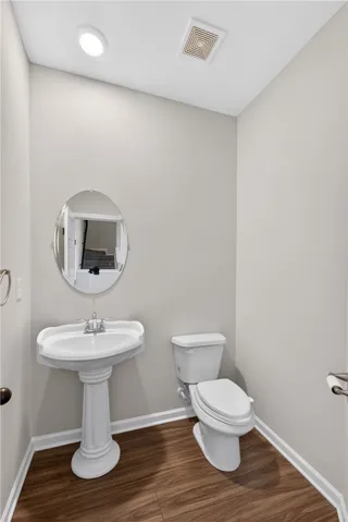 A compact powder room with wood flooring features a classic pedestal sink and an oval mirror.