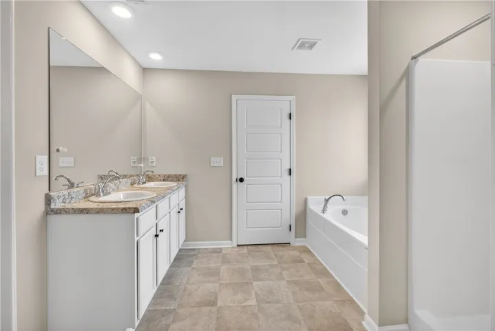 A well-lit primary bathroom featuring dual vanities and a relaxing tub with a shower.