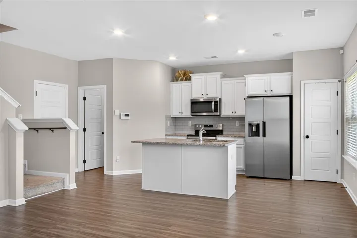 A well-lit kitchen with sleek stainless steel appliances, a generous island, and rich hardwood flooring.