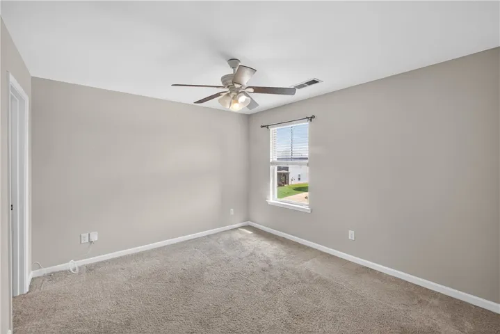 A well-lit bedroom features plush carpeting and a modern ceiling fan, inviting relaxation.