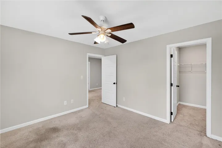 A well-lit room with plush carpeting offers comfort and a ceiling fan for climate control.