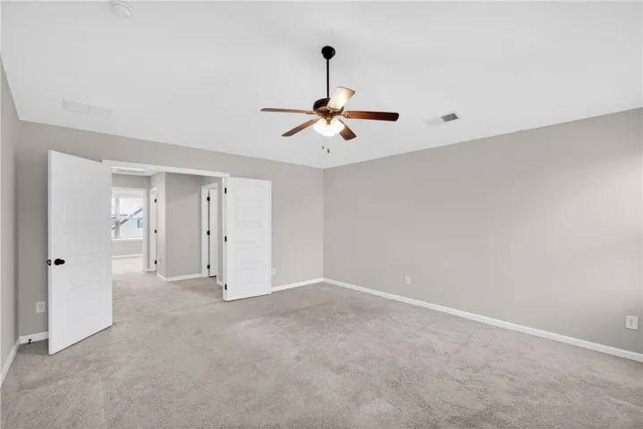 A spacious, naturally illuminated room featuring plush carpet flooring and a modern ceiling fan for comfort.