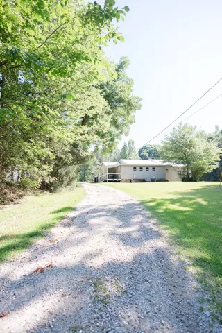 A long gravel driveway leads to a secluded home, embraced by mature trees and verdant lawns.