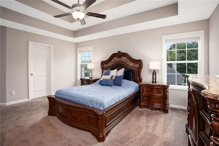 Luxurious tray ceilings and ample window light elevate this primary bedroom's comforting ambiance.