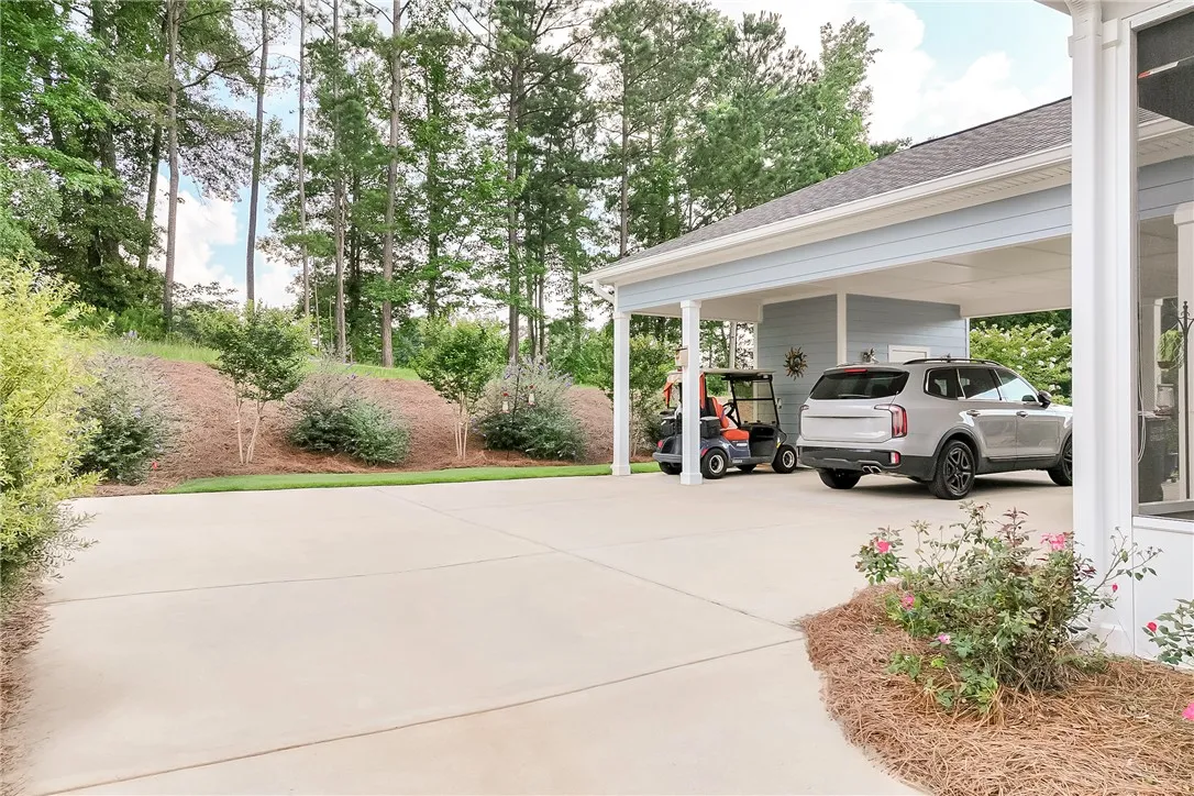 A broad concrete driveway leads to a covered carport, offering ample off-street parking.