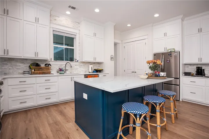 A well-appointed kitchen features a deep blue island, white cabinetry, and gleaming wood floors.