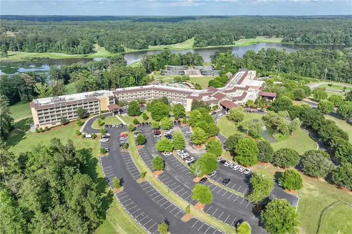 An aerial perspective reveals a vast complex amidst lush greenery, a sparkling lake, and ample parking.