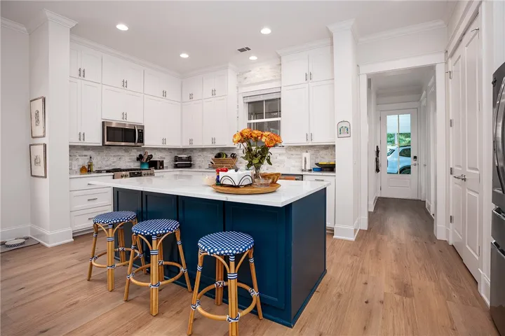 A chef's kitchen showcasing a deep blue island, white cabinetry, and gleaming wood floors.
