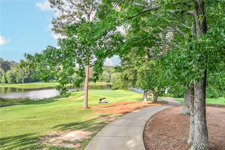 A winding path through verdant trees leads to a serene golf course alongside a tranquil lake.