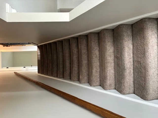 Well-lit stairway featuring a practical, carpeted tread with a warm wooden handrail.