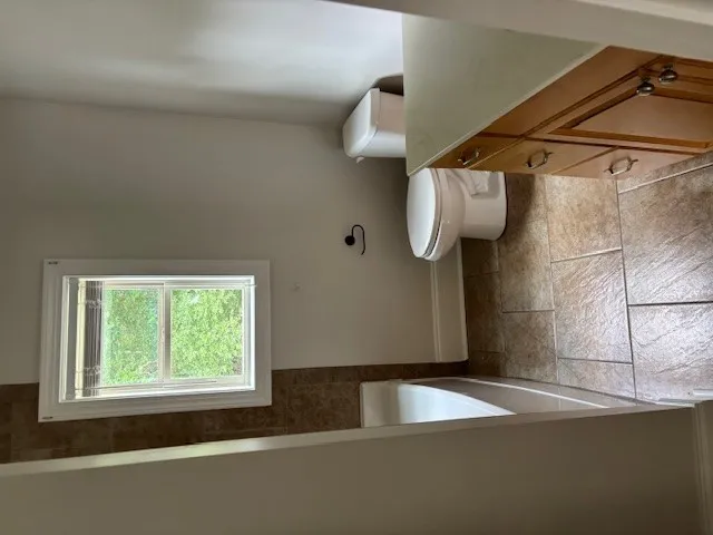 A window above the tub allows for natural light and leafy green views in this bathroom.