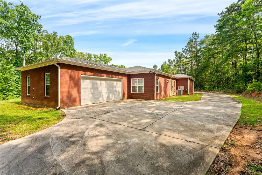 A spacious driveway welcomes you to this brick residence, nestled amidst a verdant, wooded backdrop.