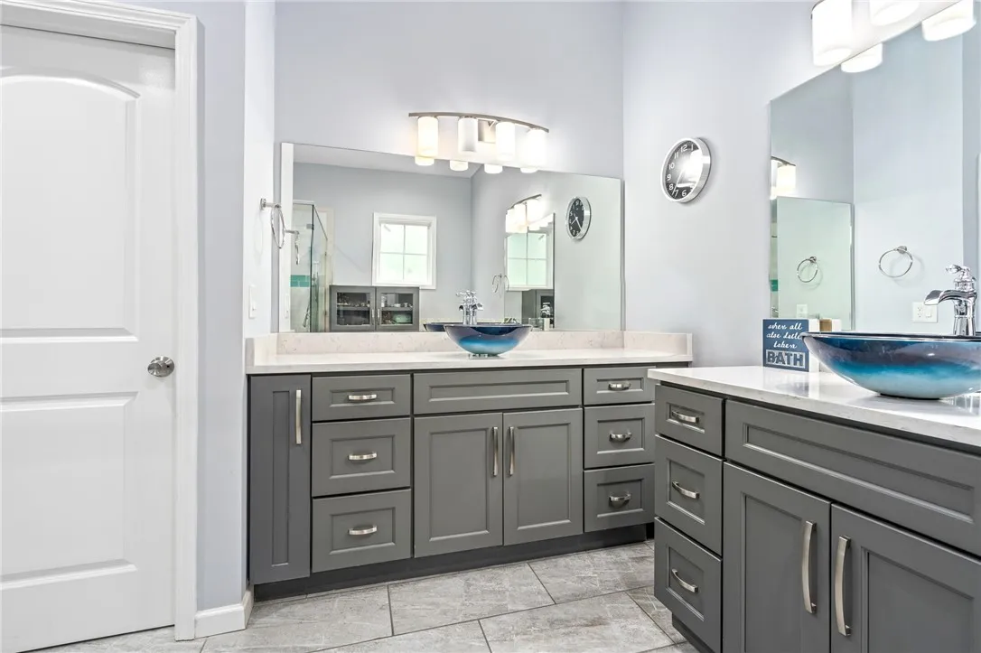 Dual vessel sinks and extensive gray cabinetry complete this elegant primary bathroom.