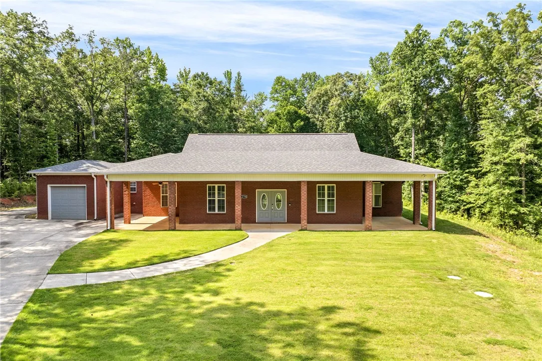 A spacious brick residence nestled among lush trees, boasting a covered front porch and an attached garage.