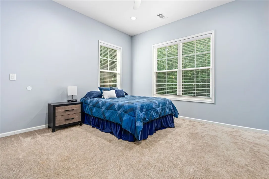A well-lit sleeping area features broad windows with verdant outdoor views and plush carpeting.