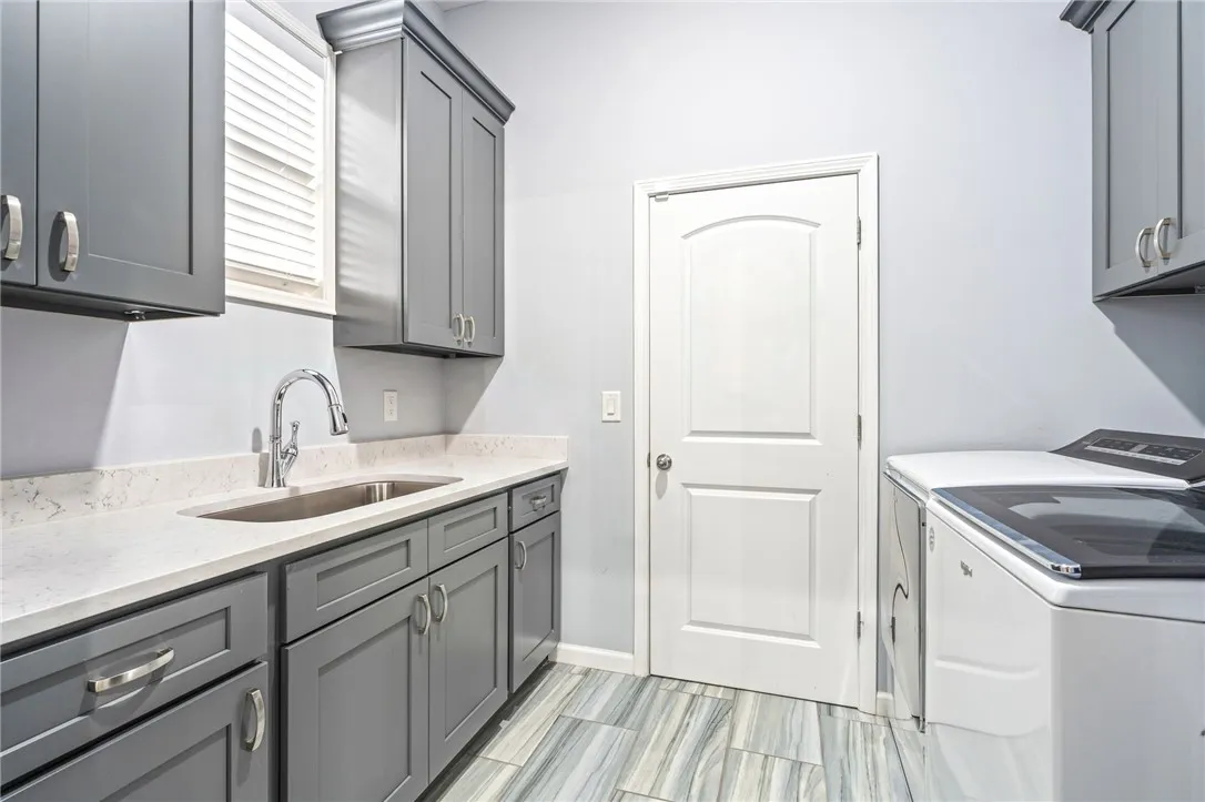 Functional laundry space featuring plentiful storage, a dedicated sink, and a clean, durable tiled floor.