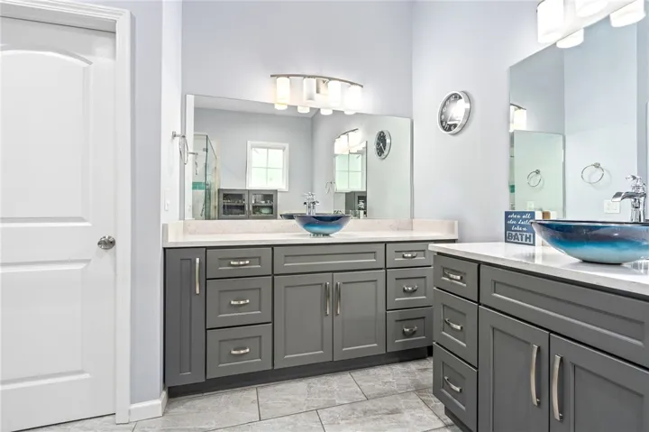 Dual vessel sinks and extensive gray cabinetry complete this elegant primary bathroom.