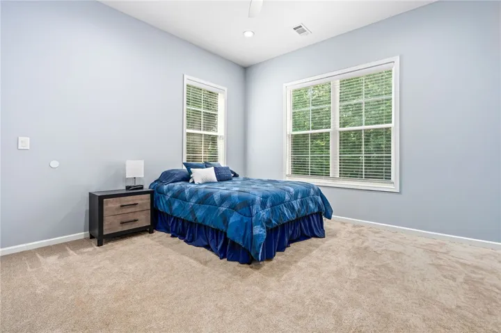 A well-lit sleeping area features broad windows with verdant outdoor views and plush carpeting.