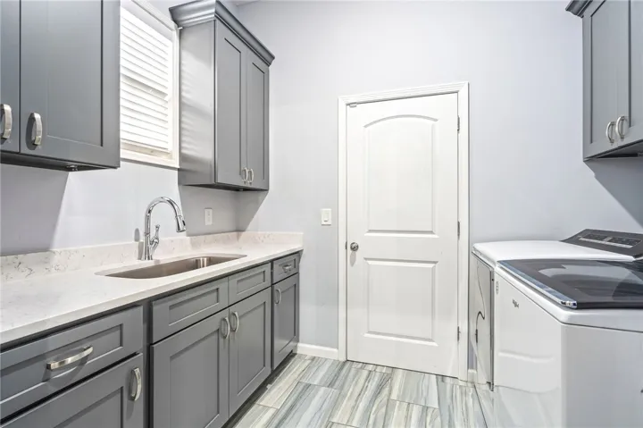 Functional laundry space featuring plentiful storage, a dedicated sink, and a clean, durable tiled floor.