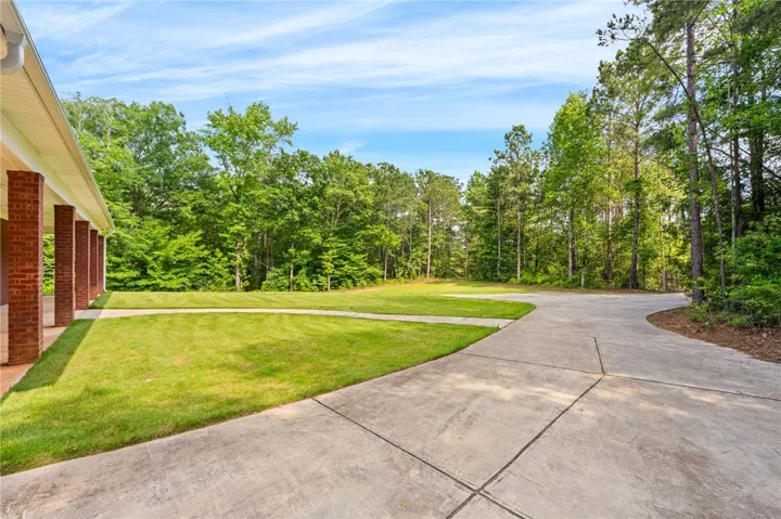A meandering driveway leads to a home surrounded by verdant trees and an expansive lawn.