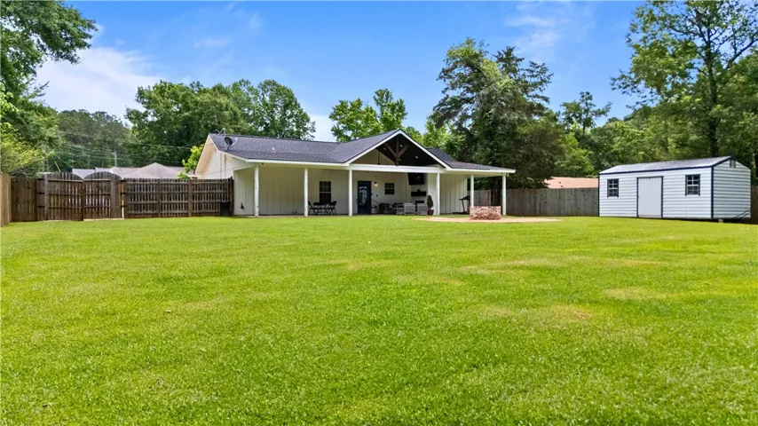 A spacious lawn unfolds to a charming home featuring a covered patio and a detached storage shed.