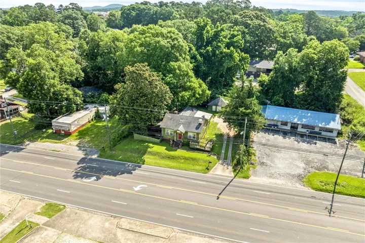 An aerial perspective reveals a charming dwelling nestled amidst a verdant landscape, bordering a busy thoroughfare.