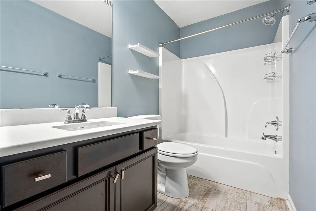 A well-maintained full bathroom featuring a tub/shower combination, dark wood vanity, and tiled floors.