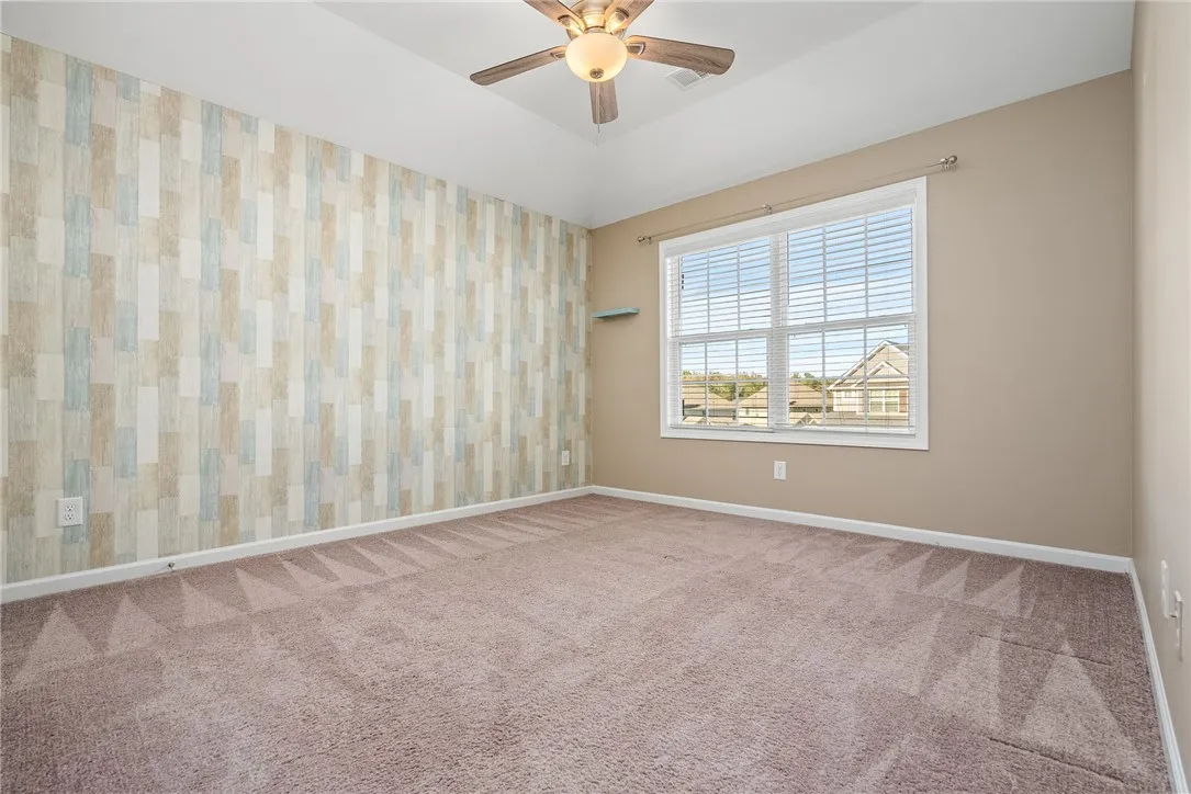 A quiet bedroom offers comfort with soft carpeting, a ceiling fan, and a view of the peaceful neighborhood.