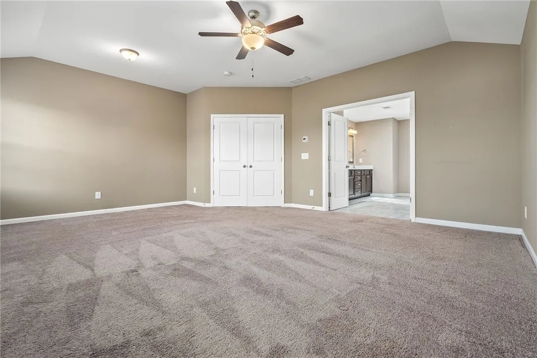 A spacious primary bedroom features soft carpeting, a ceiling fan, and convenient access to a private bathroom.