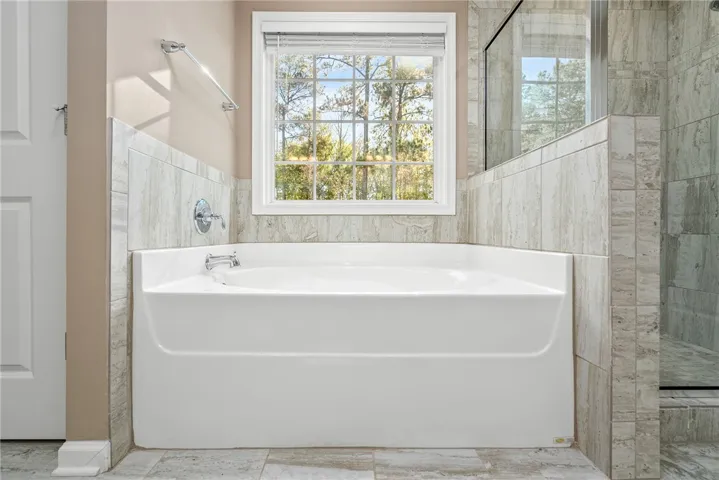 A spacious soaking tub awaits with a view to the natural surroundings, alongside a tiled shower.