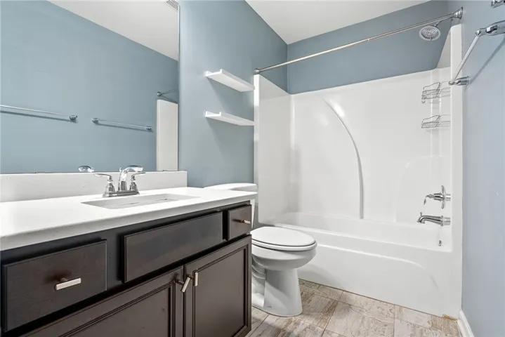 A well-maintained full bathroom featuring a tub/shower combination, dark wood vanity, and tiled floors.