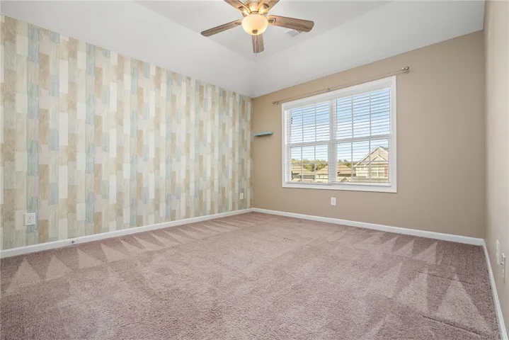 A quiet bedroom offers comfort with soft carpeting, a ceiling fan, and a view of the peaceful neighborhood.