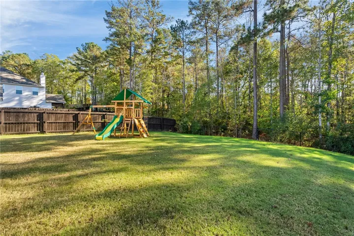 A spacious, verdant yard with a delightful playset, bordered by a privacy fence and lush woodland.