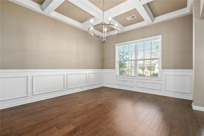 A graceful dining room presents coffered ceilings, hardwood flooring, and elegant wainscoting.