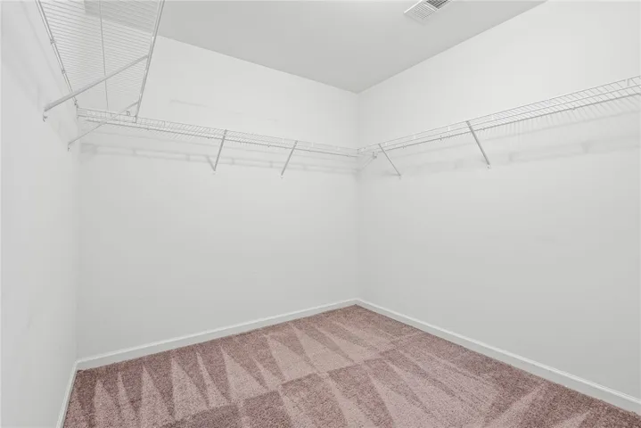 A generously sized walk-in closet with ample shelving and a patterned carpet for comfort.