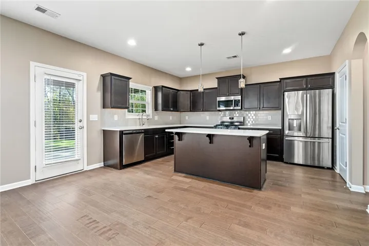 A well-appointed kitchen features dark wood cabinetry, a central island, and modern stainless steel appliances, set against light flooring.