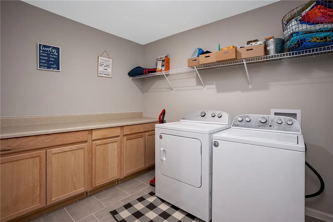 Functional laundry room equipped with generous cabinetry and overhead shelving for optimal organization.