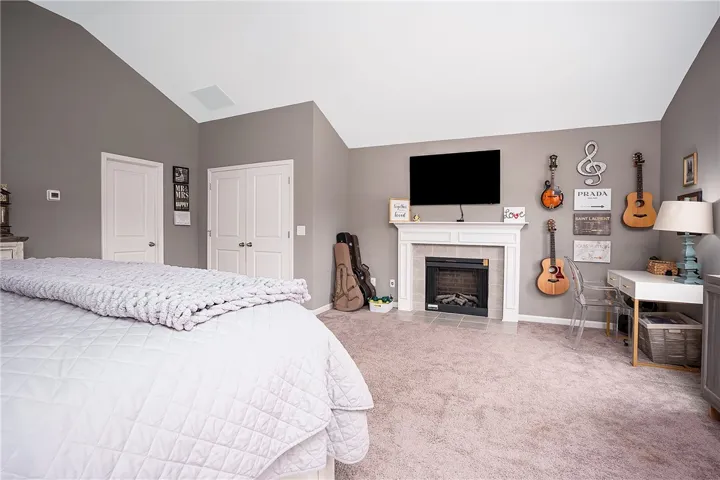 A well-lit bedroom features vaulted ceilings, soft carpeting, and a cozy fireplace, creating an inviting personal retreat.