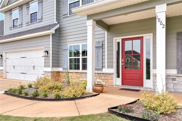 A vibrant red entry door beckons, flanked by charming window shutters and stone accents, creating an inviting facade.