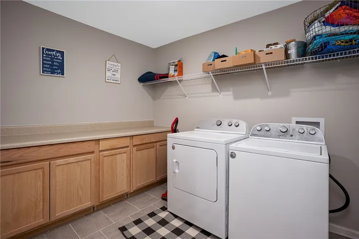 Functional laundry room equipped with generous cabinetry and overhead shelving for optimal organization.