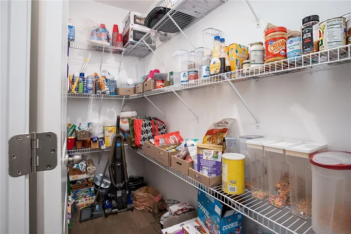 A well-organized pantry offers ample storage with tiered wire shelving and natural wood-look flooring.