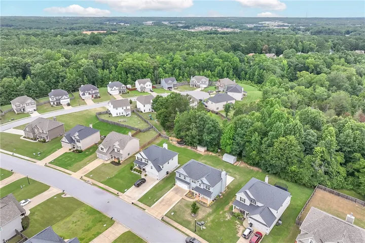 An aerial perspective reveals a serene suburban neighborhood nestled against a vibrant green forest backdrop.